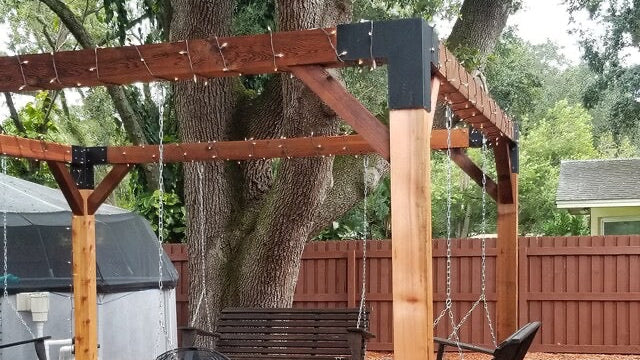 Backyard setting with wooden swing set, chairs, and fire pit under a tree.